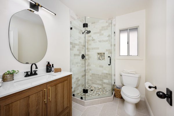 A modern bathroom interior with glass shower, wooden vanity, and white fixtures